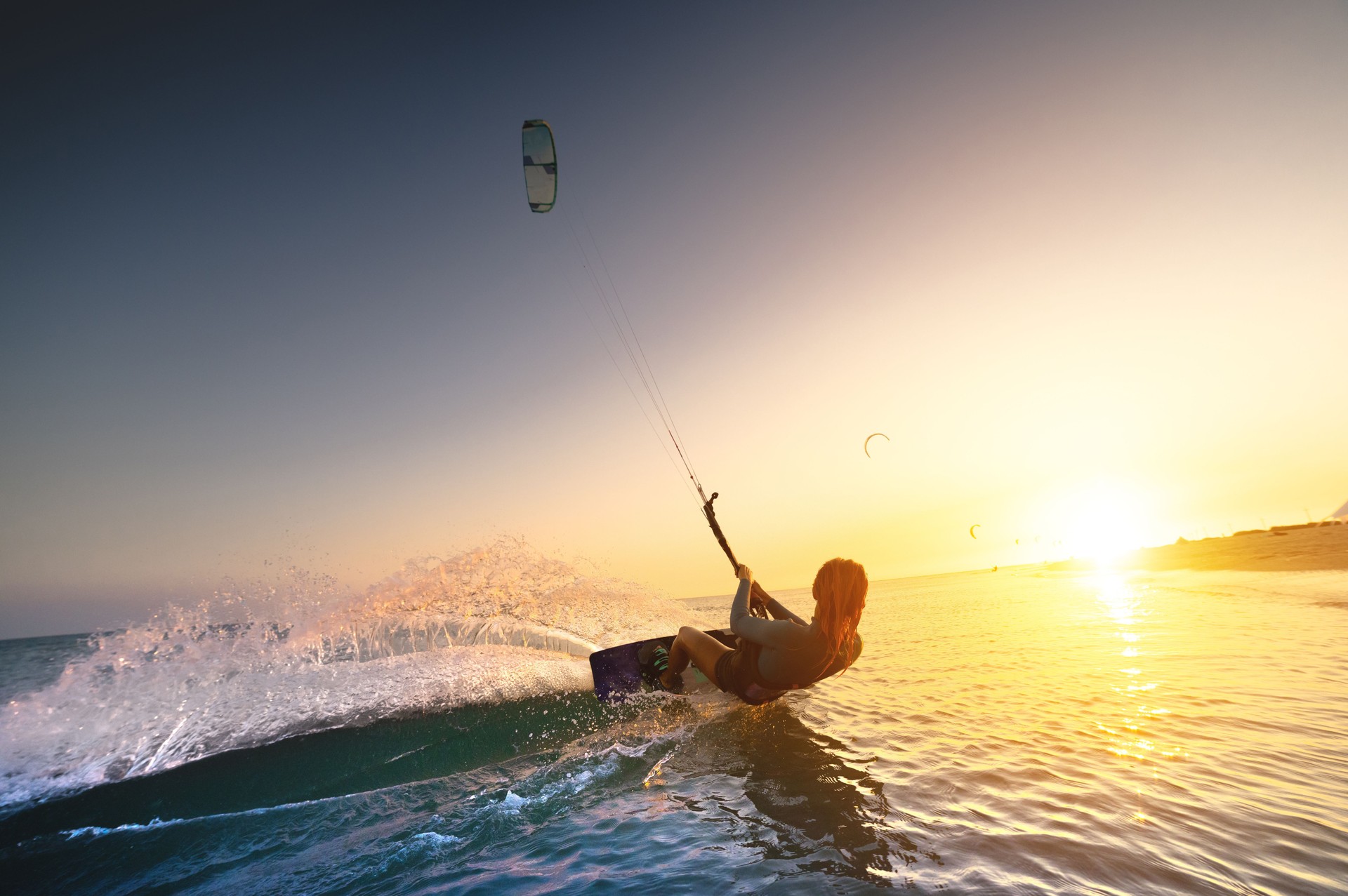 Girl Kiter se déplace sur un magnifique fond d’éclaboussures et d’un coucher de soleil coloré sur la mer. Femme kitesurf sur l’eau avec une vue fantastique en arrière-plan