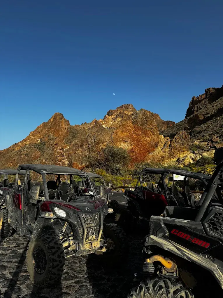 Buggies parked before a volcanic rock formation at sunset