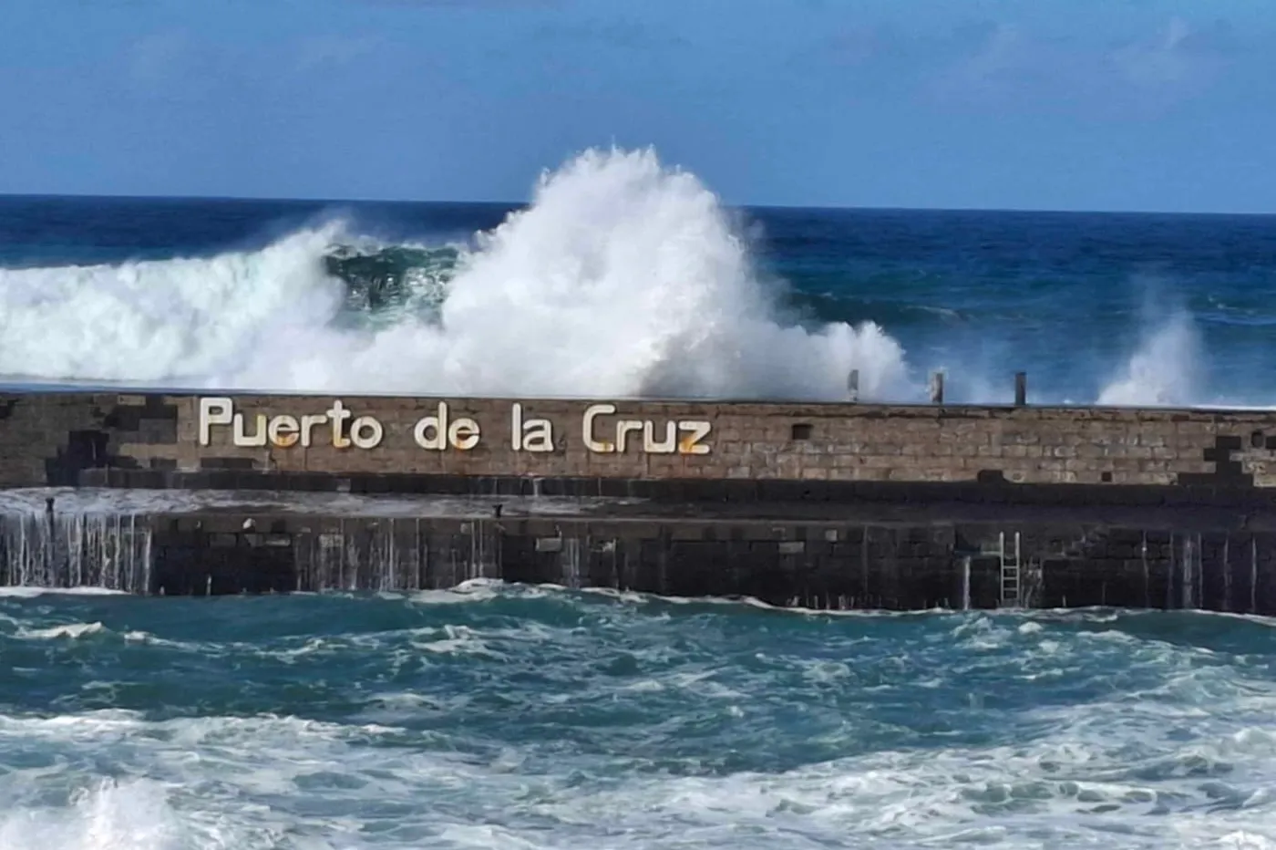 Wave breaking over the harbour wall with the Puerto de la Cruz sign
