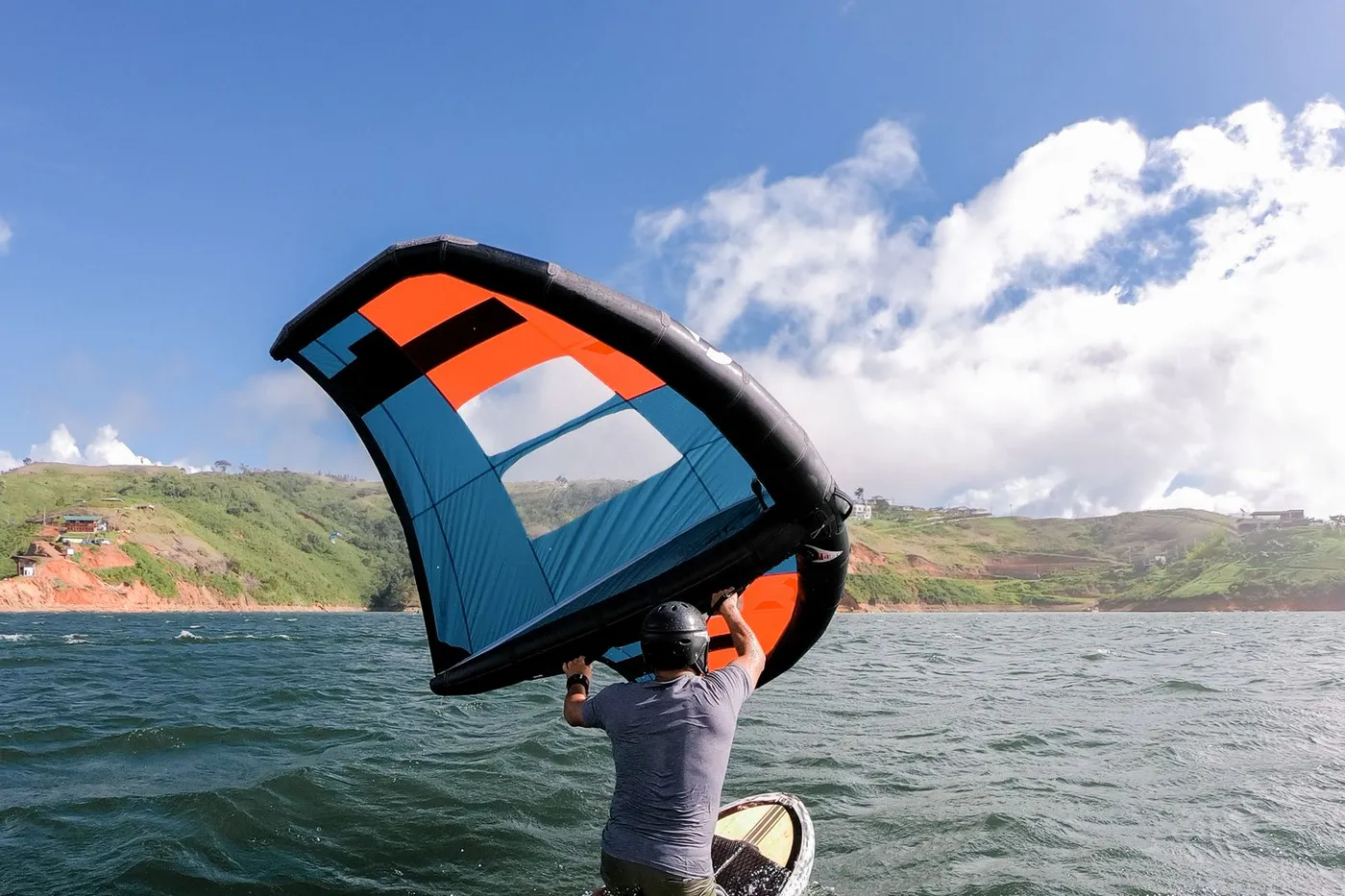 Persona practicando wingfoil con un wing naranja y negro sobre el agua